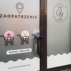 Drzwi z folią z napisem "ZAOPATRZENIE", wózkami z pączkami i logo cukierni.