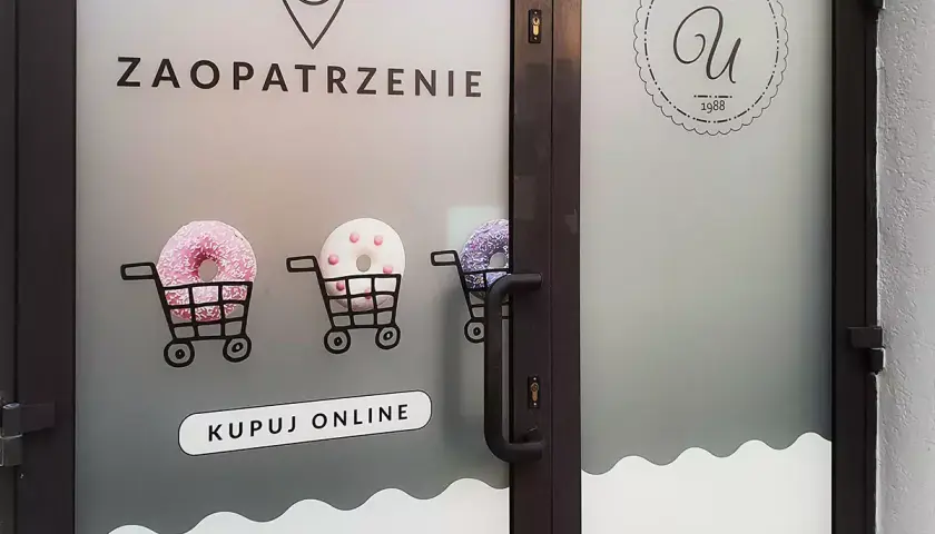 Drzwi z folią z napisem "ZAOPATRZENIE", wózkami z pączkami i logo cukierni.