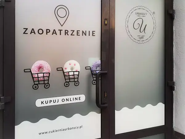 Drzwi z folią z napisem "ZAOPATRZENIE", wózkami z pączkami i logo cukierni.